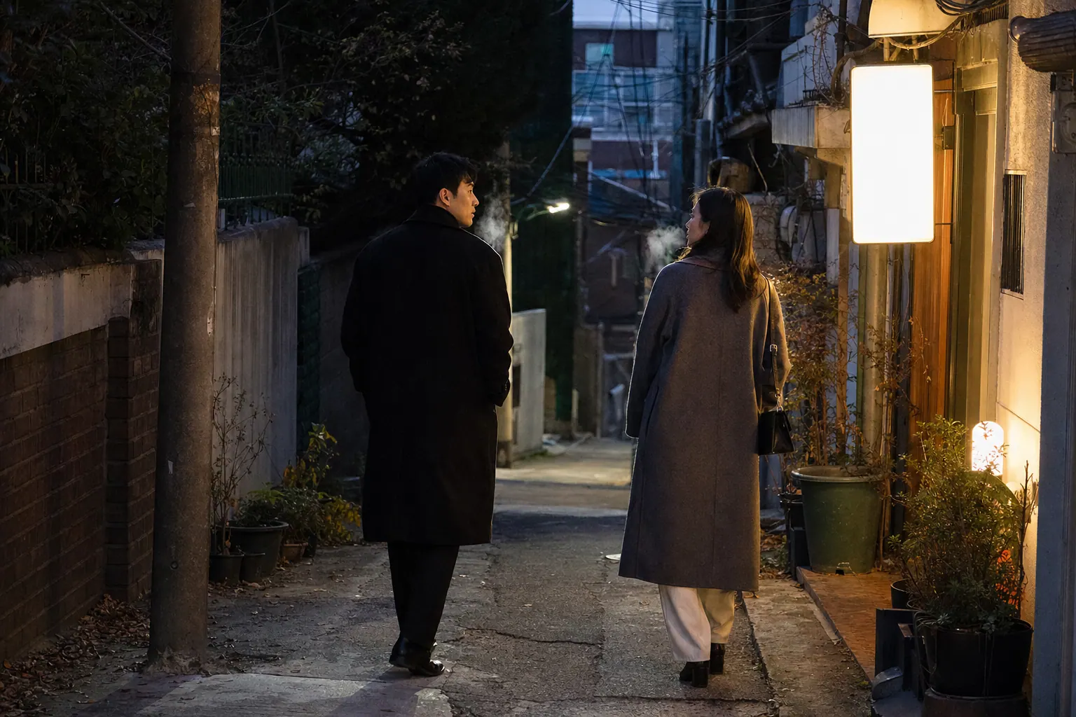 A documentary photograph of a couple leaving a small consultation office at dusk in autumn, walking a half step apart down a narrow Seoul alley lit by a single shop sign, their breath visible in the cold air, one glancing back toward the other.
